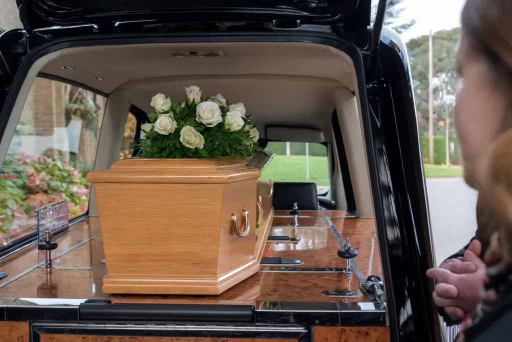 Cercueil en bois dans le corbillard avec un bouquet de roses blanches.
