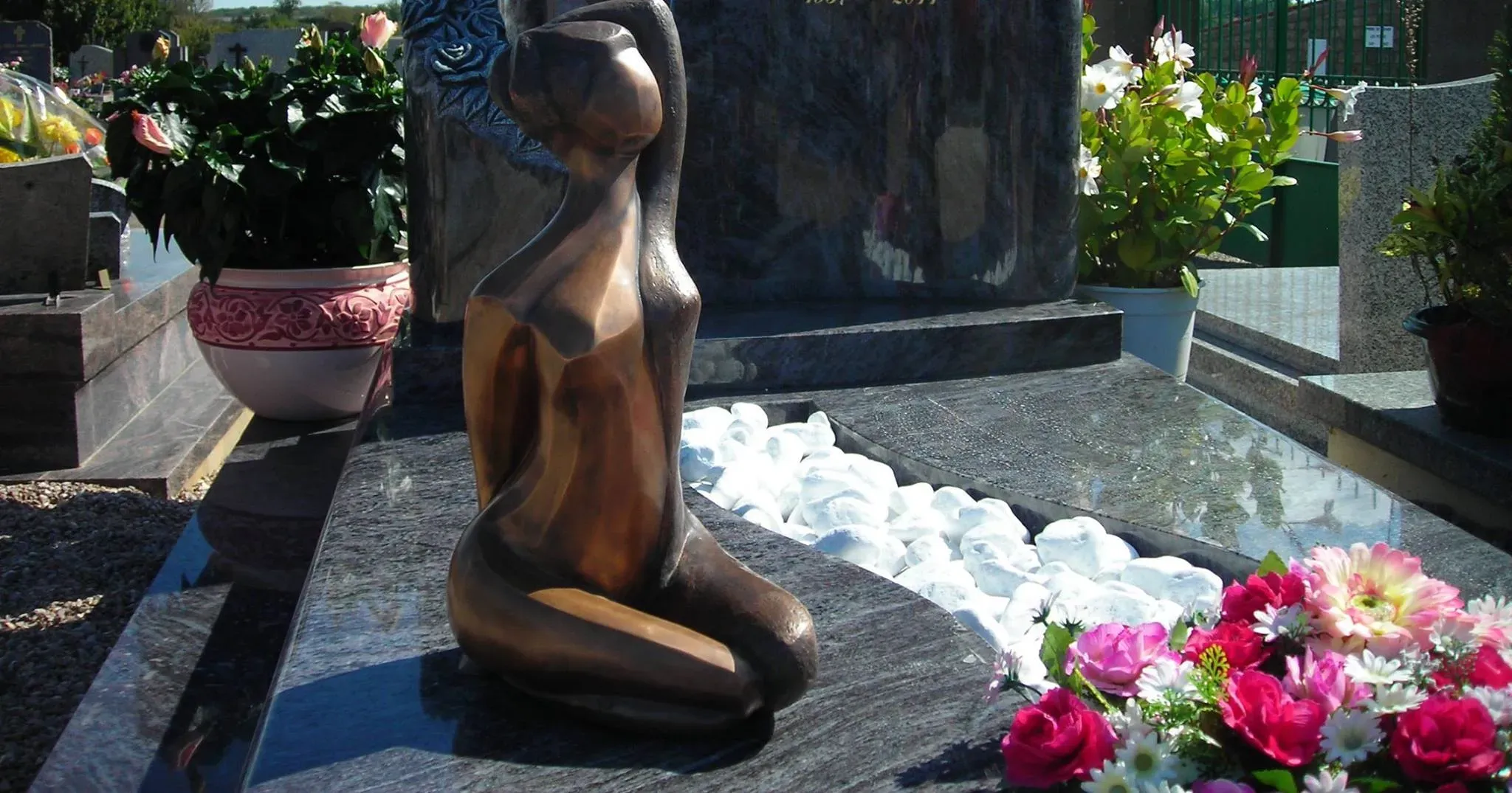 Sculpture moderne en bronze posée sur une tombe décorée de fleurs.