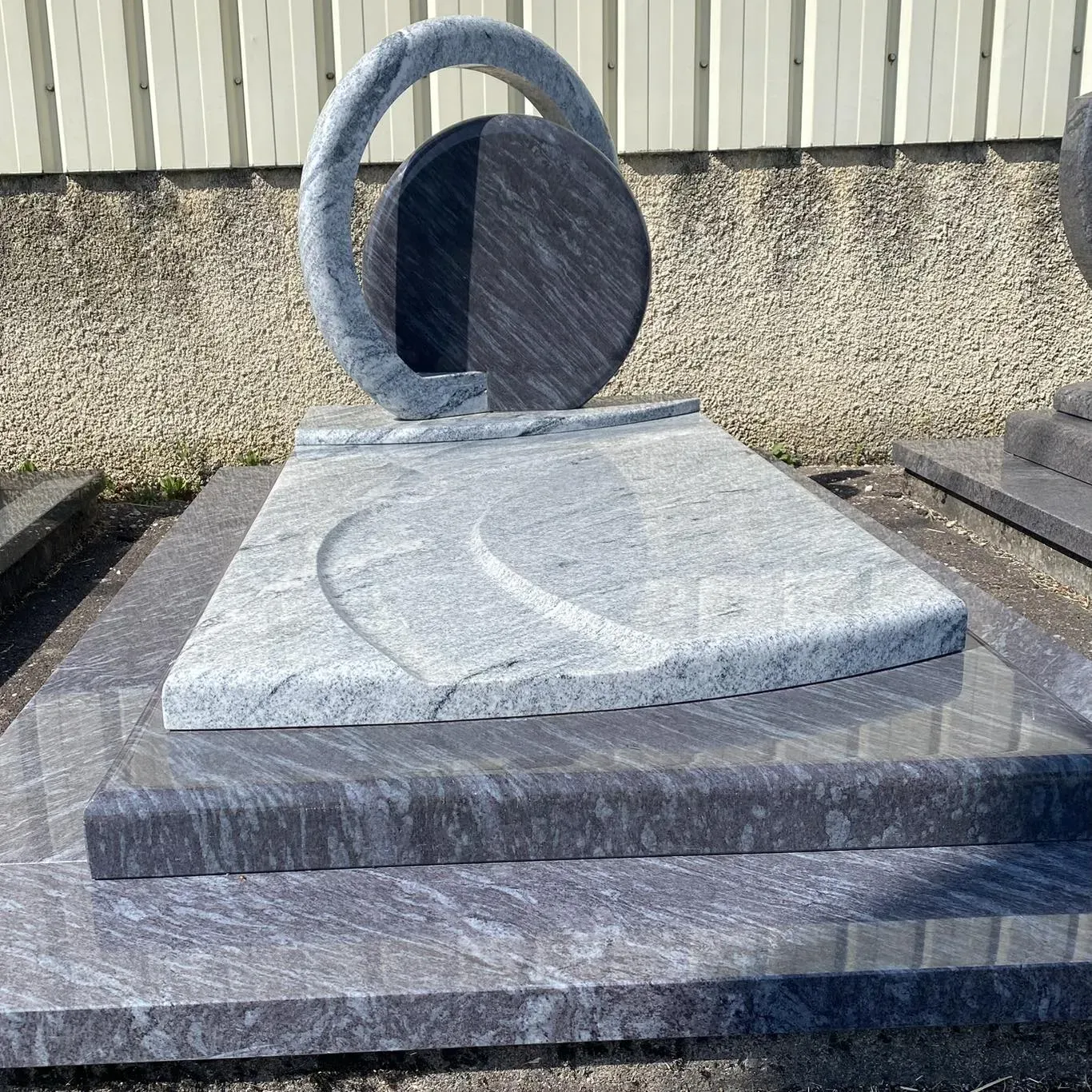 Monument funéraire contemporain en granit gris clair veiné avec stèle circulaire sculptée.