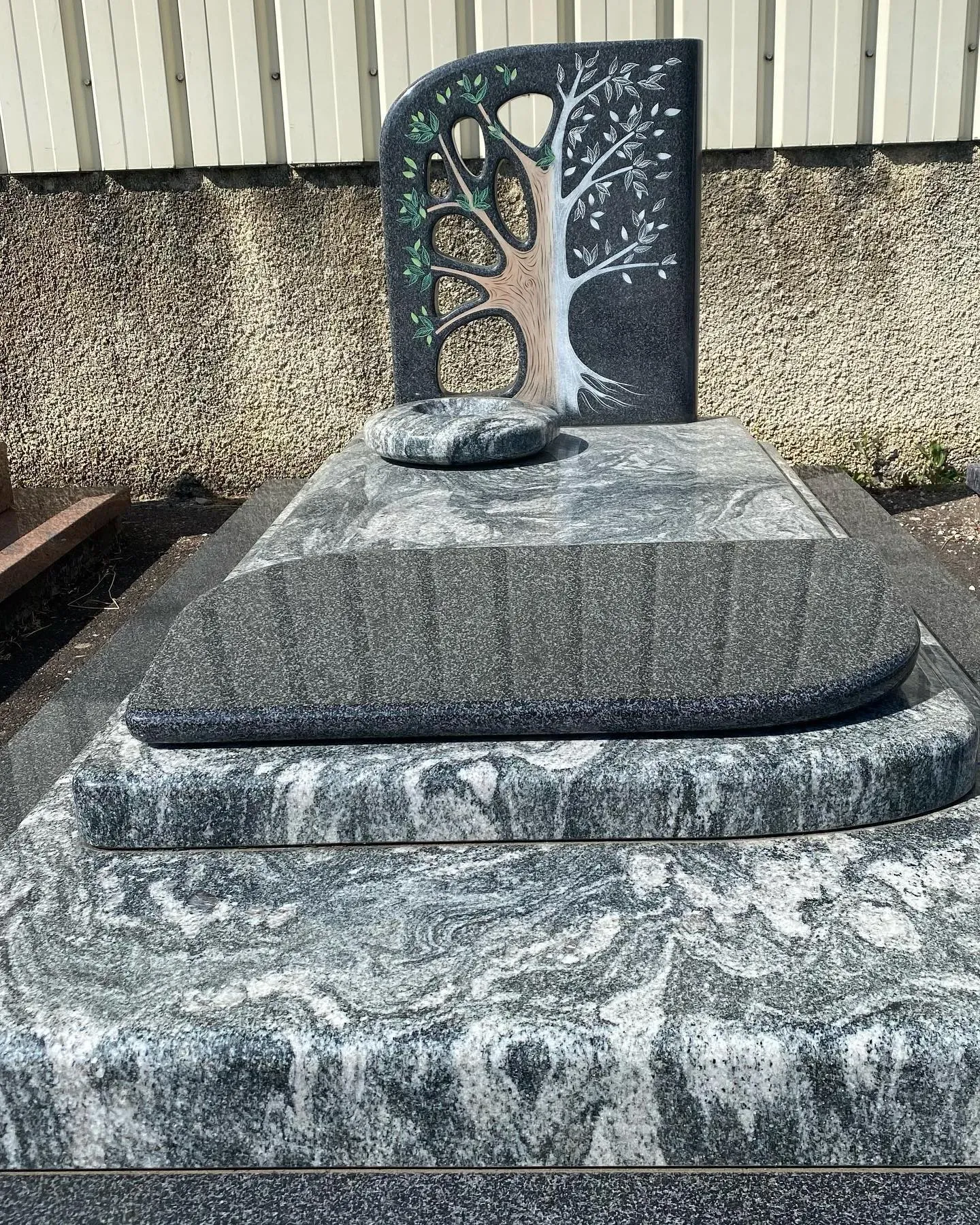 Monument funéraire en granit gris veiné avec stèle gravée représentant l'arbre de vie.