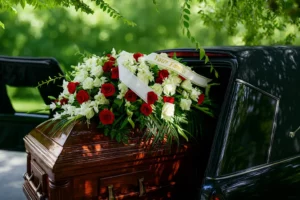 Cercueil en bois poli dans un corbillard, orné de roses rouges et blanches.