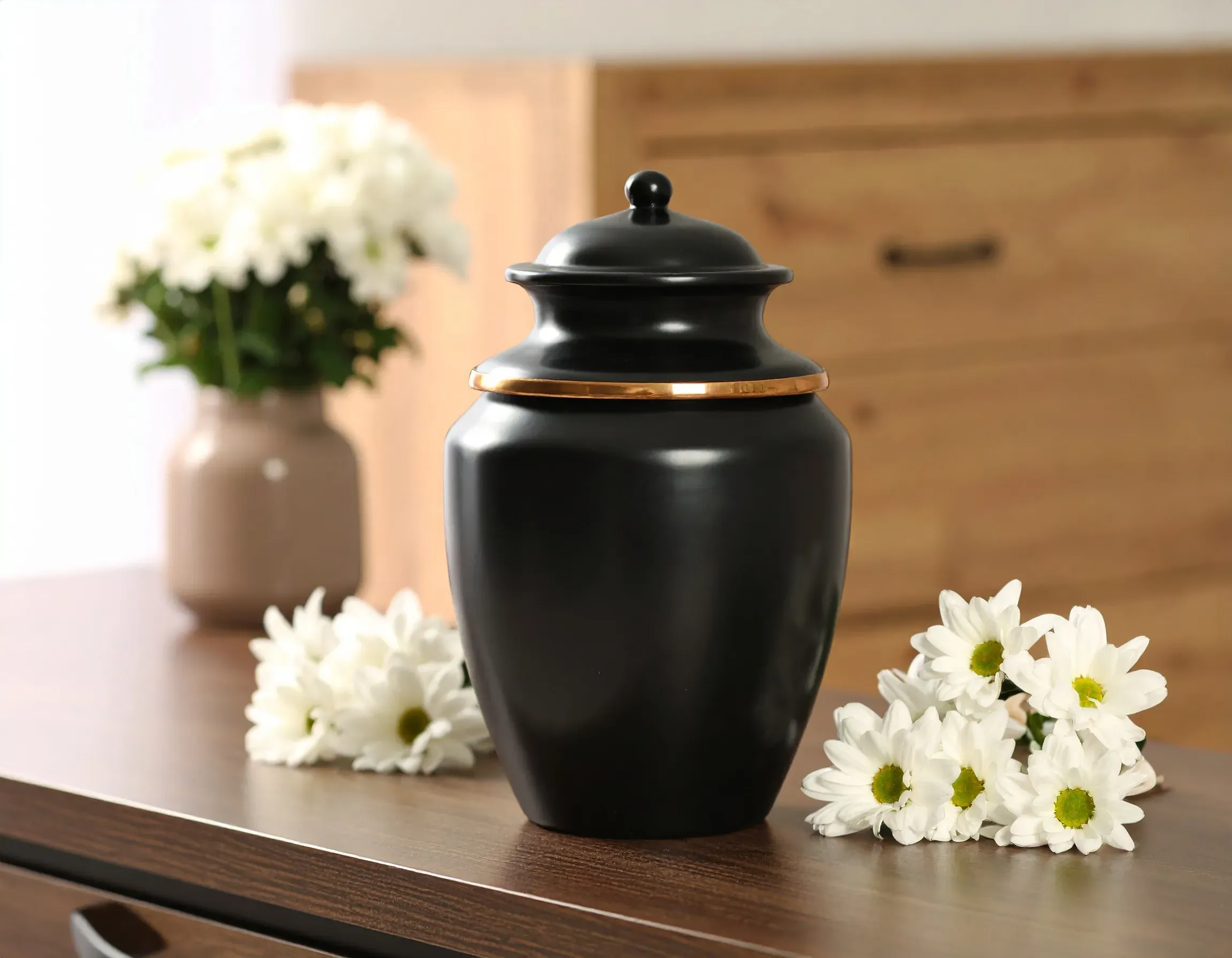 Urne funéraire noire avec liseré doré, entourée de chrysanthèmes blancs.