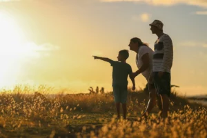 Silhouette d'une famille admirant un coucher de soleil en plein air.