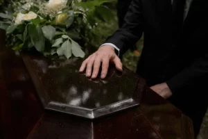 Gros plan sur la main d'un homme endeuillé posée sur un cercueil en bois brillant.